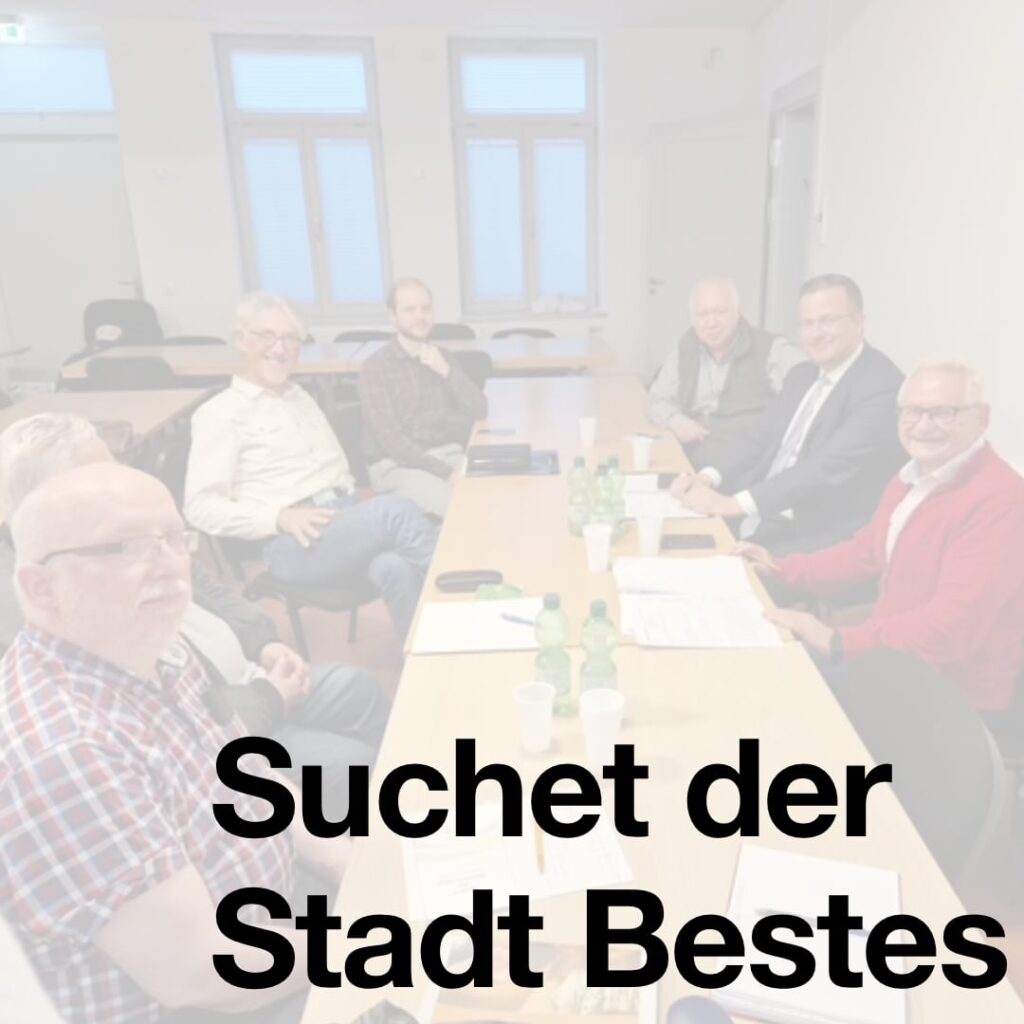 Bild zeigt mehrere Personen an einem Tisch, die freundlich in die Kamera schauen. Text: Suchet der Stadt Bestes.
