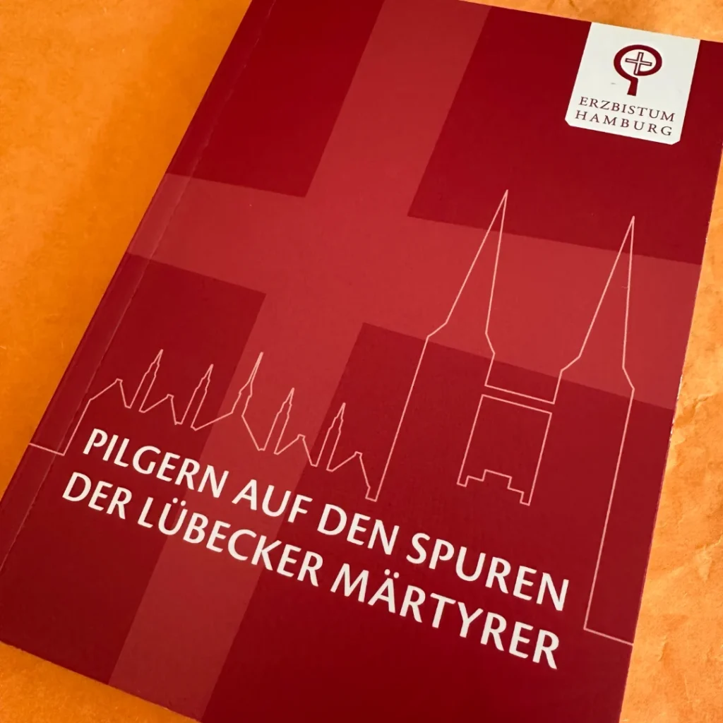 Das Bild zeigt die Titelseite des postkartengroßen Pilgerbuches. Oben rechts das Logo des Erzbistums Hanburg, darunter die Silhouette der Lübecker Kirche Herz Jesu. Text: Pilgern auf den Spuren der Lübecker Märtyrer.