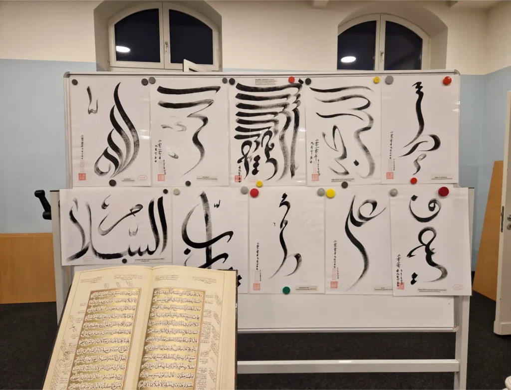 Das Bild zeigt eine Stellwand, auf der übergroße Schriftzeichen aus dem Koran stehen.