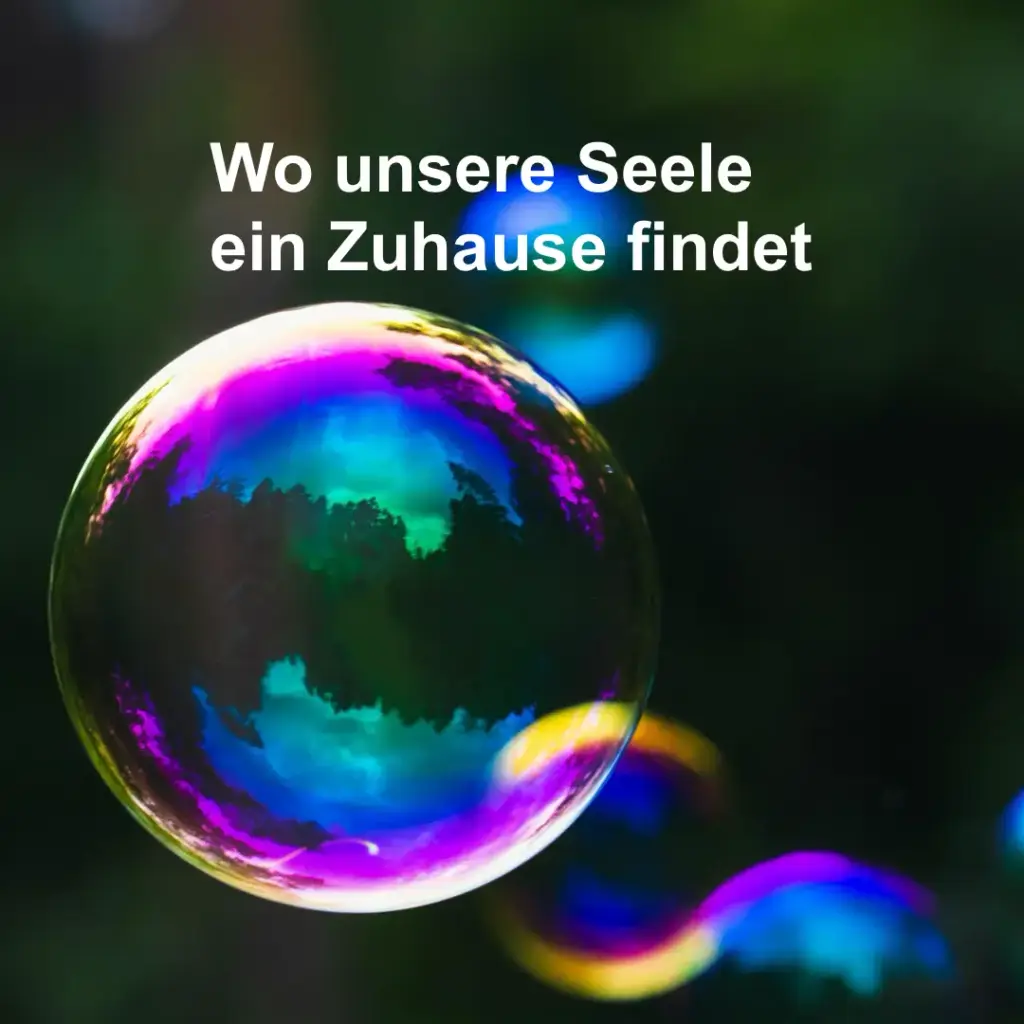 Das Bild zeigt mehrere bunt schillernde Seifenblasen vor schwarzem Hintergrund. Text: "Wo unsere Seele ein Zuhause findet".